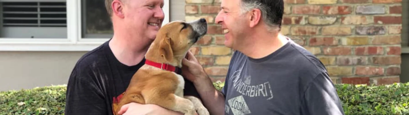 two men holding and smiling at happy pup